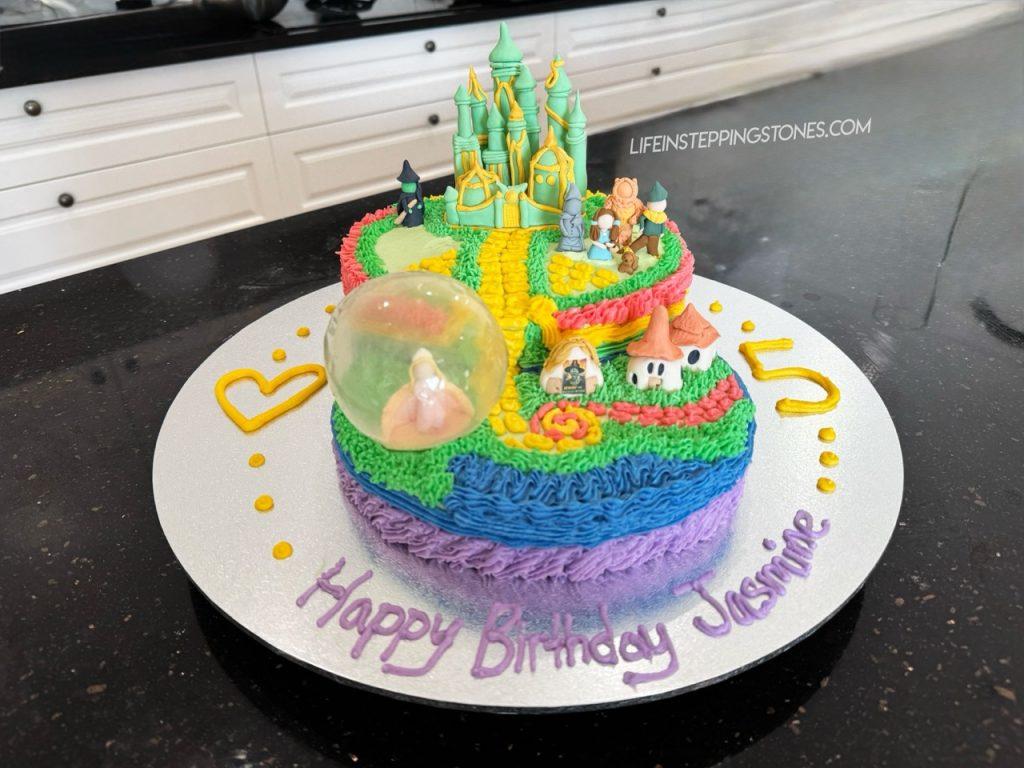 Wicked birthday cake with Glinda in her bubble, the Wizard of Oz group walking to Emerald City, and Elphaba watching from the background.